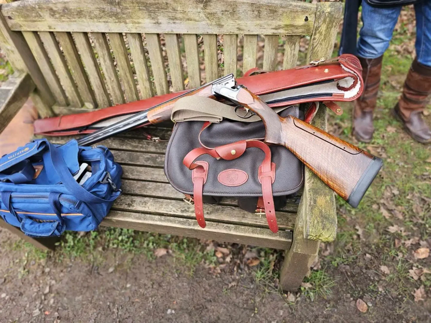 Leather bag and gun slip on a wooden bench.
