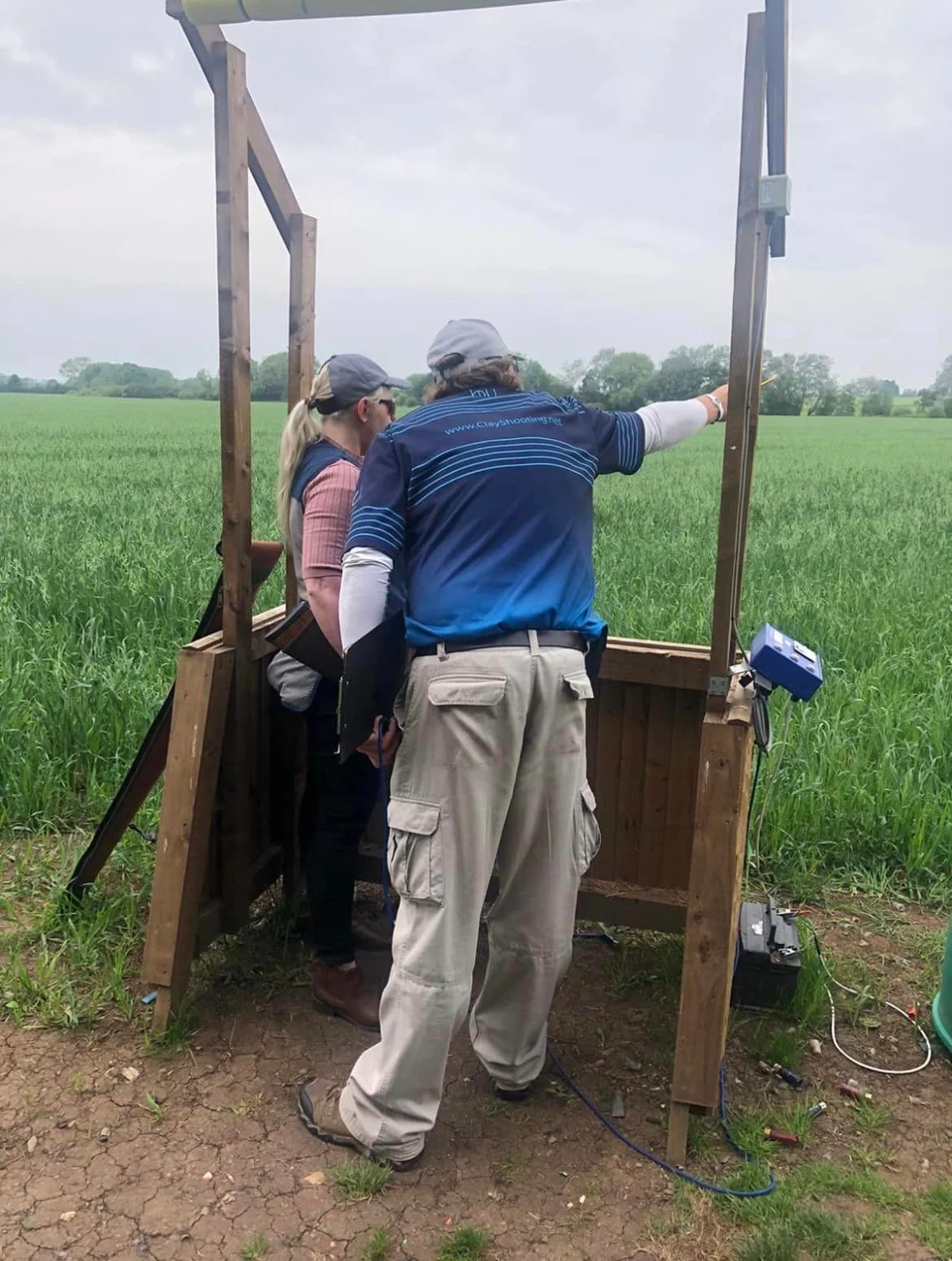 An instructor assisting a shooter inside a wooden clay stand.