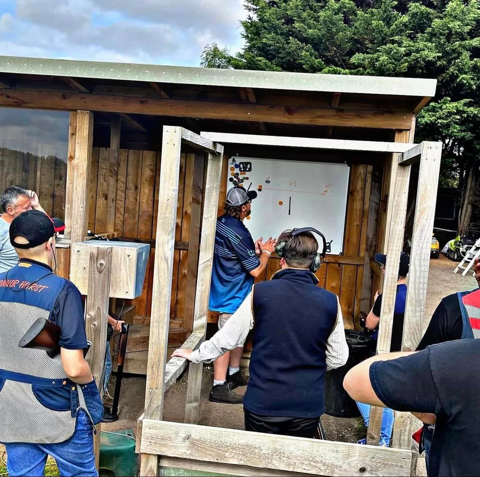 Shooters gathered around a wooden clay shooting stand.